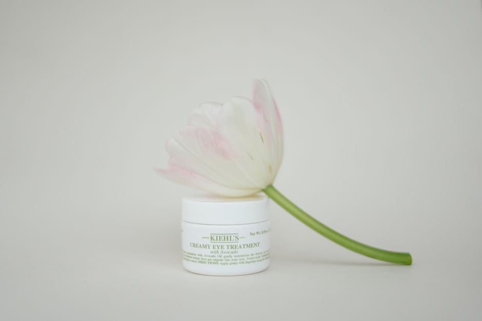 A tulip elegantly draped over a luxurious creamy eye treatment container on a white background.