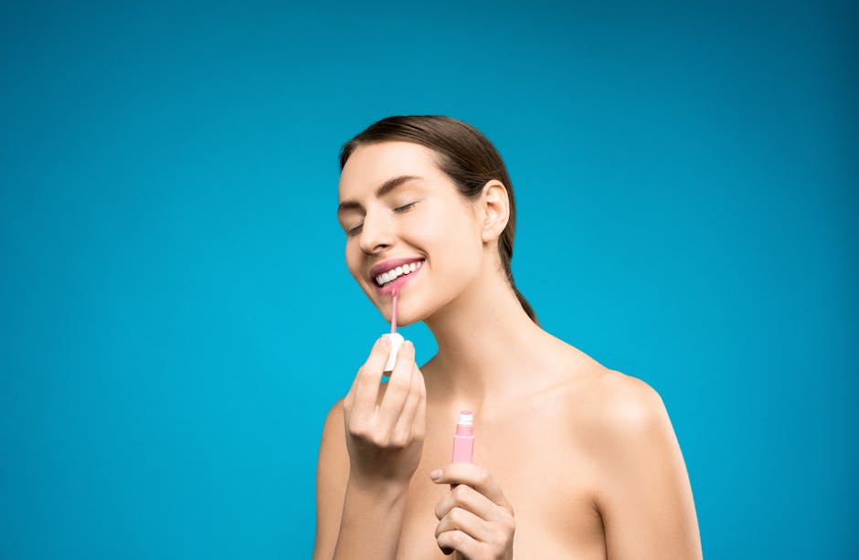 A joyful woman applies pink lipstick against a bright blue backdrop, exuding beauty and confidence.