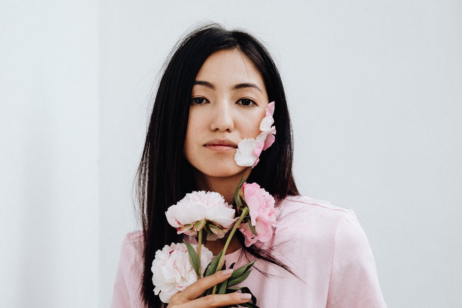 Close-up of an Asian woman holding pink flowers against a plain background.