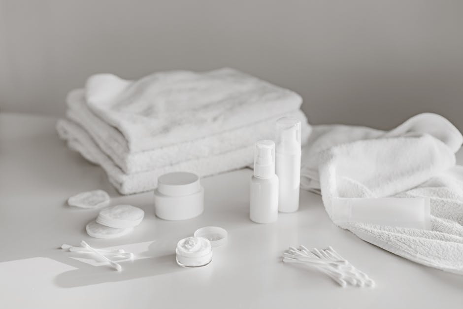 A neat arrangement of white skincare products and towels on a clean surface, perfect for spa and beauty themes.