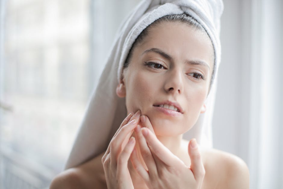 Young woman with towel examining her face during skincare routine in a bathroom setting.