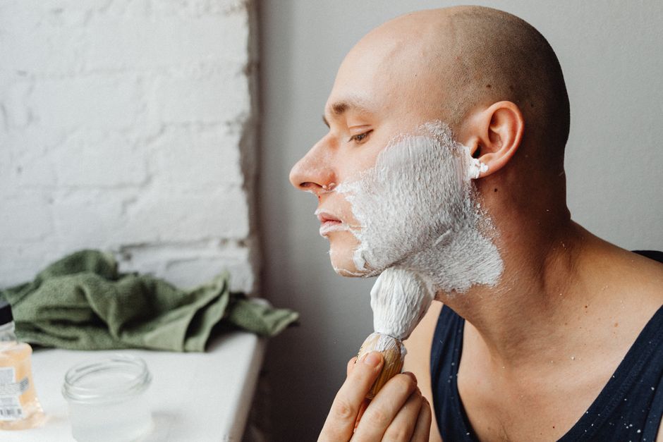 Close-up of a bald man shaving with cream from a side view in a bathroom setting.