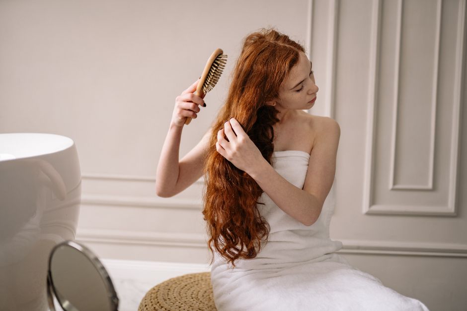 Woman with long red hair wrapped in a towel combing her hair in an elegant bathroom setting.