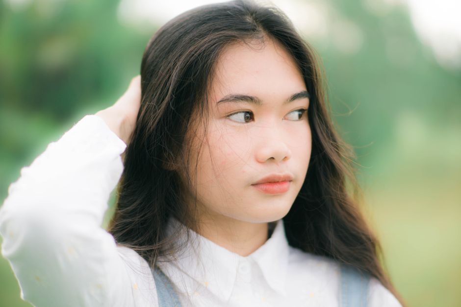 Close-up of a young woman with long hair and a serene expression, outdoors in natural light.