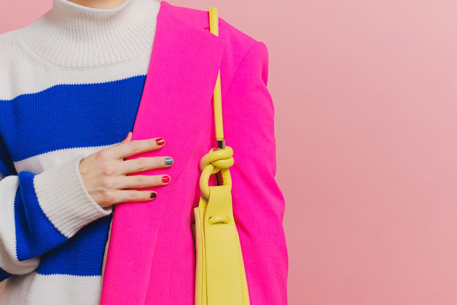 Vibrant image showcasing a stylish pink blazer paired with a yellow shoulder bag and colorful nails against a pink background.