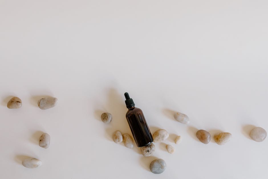 Brown essential oil dropper bottle surrounded by smooth stones on a white surface, highlighting simplicity.