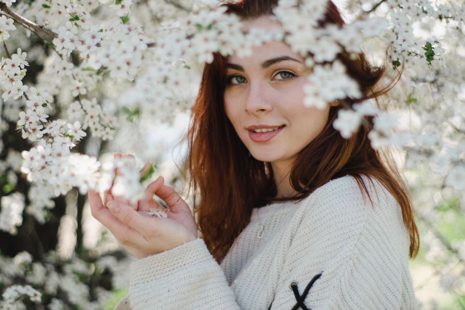 Young woman in spring, smiling gently, surrounded by blossom flowers.
