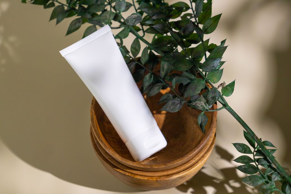 Minimalist skincare tube with green leaves in a wooden bowl, ideal for eco-friendly cosmetic themes.